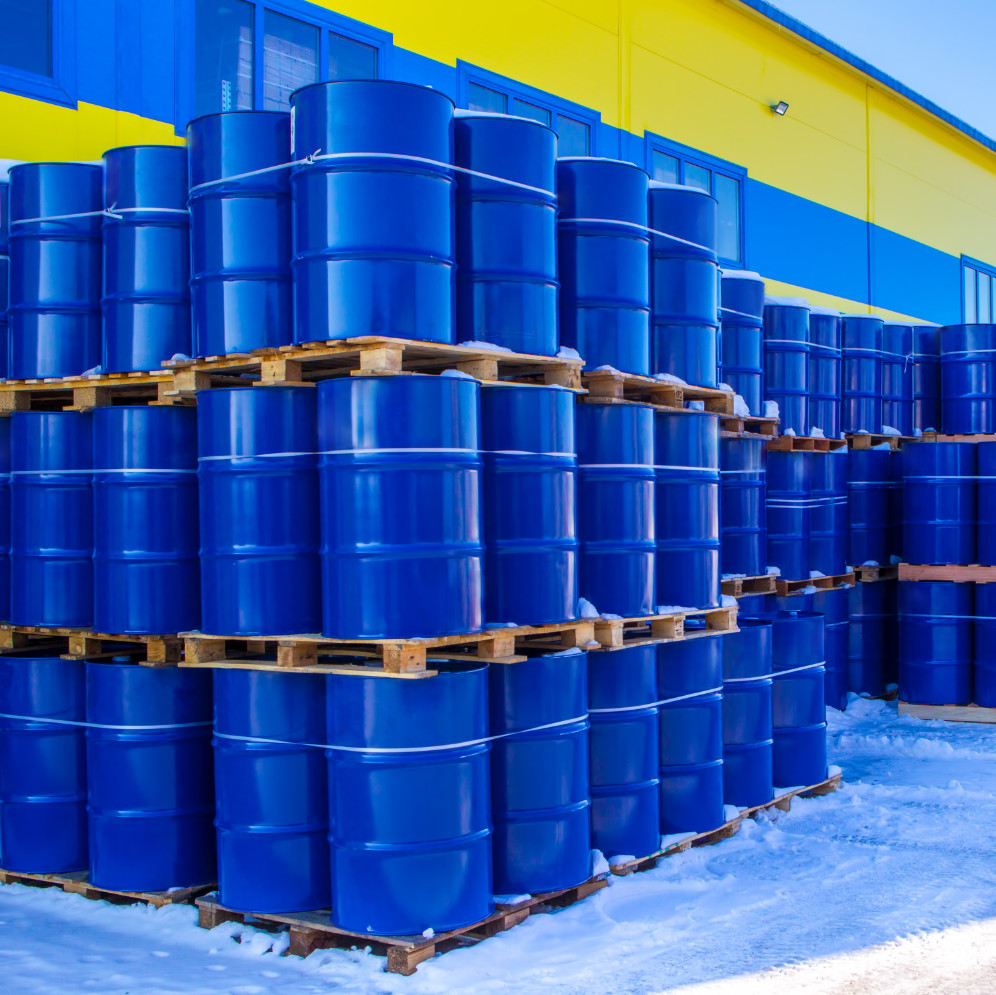 Blue containers are palletized in stock. Metal barrels for chemicals.
