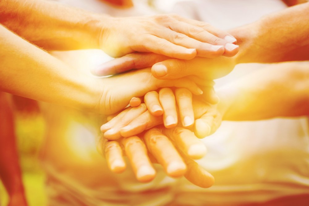 Happy volunteer family putting their hands together on a sunny day.